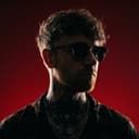 Danny Stuart in sunglasses and a patterned shirt, lit red against a deep red background.